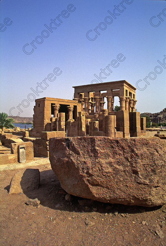 Philae Temple EG20481jhp 
 Philae Temple Egypt Kiosk Trajan large boulder granite Hathor island Agilkia was established late in the history of Egypt being mainly Ptolemaic, eventually closing as a religious site around 550AD and being located on an island had remained remarkably untouched, partly as it was submerged when the Nile flooded after the construction of the first dam. Being relocated onto the Island of Agilkia on the River Nile near Aswan, to save it being flooded permanently after the completion of the High Dam, it is perhaps one of the loveliest and most complete classic Egyptian temples to visit with a peaceful spirituality lacking in many of the land based sites mainly because of being isolated on an island from modern day noise and often being less crowded as less accessible. It also has a very delightful Light and Sound show, partly a walk through to the Sanctuary followed by a sit down session just past the Kiosk of Trajan. 
 Keywords: Egypt, Aswan, River Nile, Nubia, Philae Temple, island, pylons, carvings, Ptolemy, Ptolemaic, Isis, cult, relocated, rescued, High Dam, landscape, upright, history, ancient, Egyptian, antiquity, entrance, pylon, first, Ptolemy, second, granite, stele, year, 24, Philometer V11, mammisi, birth, house, chapel, kiosk, Trajan, lion, colonnade, columns, Roman, archaeology, Egyptology, Agilkia, Island, gate, Diocletian, Augustus, temple, Hathor, steps, water, motorboat, water, beautiful, serene, peaceful, oleander, flowering, flowers, July, 2000, slide, film, Fuji, Velvia, Nikon, FM2, FG20, manual, 35mm, scanned, scan