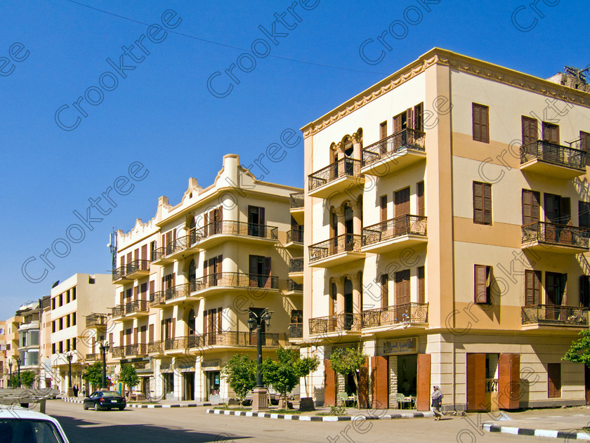 Luxor Street Architecture EG072590jhp 
 Egyptian Luxor street residential flats apartments balconies stylish modern architecture Egyptian influence found along this long straight road Sharia al-Mahatta from just behind Luxor Temple and facing the elegant and modern railway station faade. We were dropped here before entering the station and boarding the main Aswan to Cairo train for a visit to the Minya area. One aspect of the traffic management that I thoroughly approved were the traffic lights at junctions with a clock showing how soon to the change of lights. 
 Keywords: Egypt, Thebes, Luxor, Waset, Ipetisut, East, Bank, River, Nile, Sharia, al Mahatta, landscape, road, station, platform, train, railway, Ramses, waterfront, promenade, esplanade, Corniche, modern, architecture, European, influence, style, stylish, balconies, Egyptian, theme, eye, wedjat, freize, cornice, construction, apartment, block, street, cars, people, tree-lined