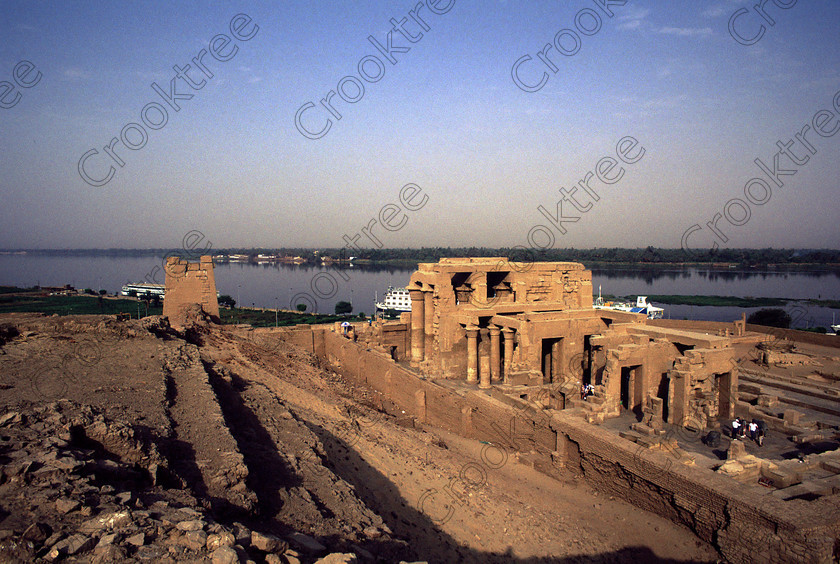 Kom Ombo EG20434jhp 
 Kom Ombo Temple River Nile Egypt rare high view upstream vista of this beautiful ruined temple just north of Aswan and a regular visit on all Nile Cruises, was principally built by Ptolemy V of Silsilah sandstone. Dedicated to two Gods  Sobek, the crocodile and Horus, the falcon and although it has been damaged over the years, mainly through slipping into the River Nile and some structural damage owing to earthquakes, there are still some wonderful colourful reliefs of the most detailed and delicate style. This trip was special for me in that I got special permission to climb up the back of the temple on the hill behind and match a view I had on a Victorian albumen print; the local Police Chief had to be involved and thanks to a good Kuoni Guide he agreed for me to be accompanied by a policemen as security was still a big thing after the 1997 attacks at Luxor. Unfortunately in the excitement I had forgot to adjust my ASA rating for Velvia and took the photos based on 400ASA-the film maws later pushed to 200asa so there is some increase in grain structure, not a feature of Velvia generally. On this visit some cleaning and restoration was being done to the many painted bas reliefs on the columns-hence the scaffolding and the sun umbrella but the bonus was the reliefs looked particularly vibrant. The time of day also meant some of the museum blocks with deep cut carvings were ideal to photograph as the shadows gave greater emphasis to the excellent cut marks of some iconic hieroglyphic symbols. 
 Keywords: Egypt, East Bank, River Nile, Kom Ombo, Temple, summer, morning, hypostyle hall, pylon, columns, bas, reliefs, restoration, cleaning, conservation, coloured, colored, colours, colors, Silsilah, sandstone, landscape, history, archaeology, ancient, Egyptian, Egyptology, crocodiles, Ptolemaic, Ptolemy, Horus, Haroeris, Harwer, Sobek, Hathor, carvings, detailed, delicate, beautiful, fine, Velvia, slide, film, scans, scan, scanned, 35mm, Nikon, FM, manual, July, 2000