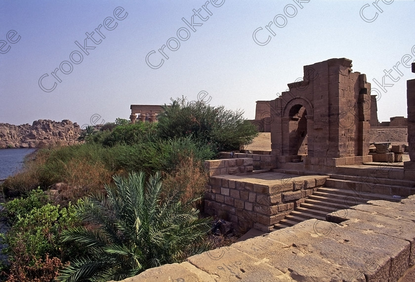 Philae Temple EG204533jhp 
 Philae Temple Egyptian Gate steps Diocletian quay east end Agilkia island was established late in the history of Egypt being mainly Ptolemaic, eventually closing as a religious site around 550AD and being located on an island had remained remarkably untouched, partly as it was submerged when the Nile flooded after the construction of the first dam. Being relocated onto the Island of Agilkia on the River Nile near Aswan, to save it being flooded permanently after the completion of the High Dam, it is perhaps one of the loveliest and most complete classic Egyptian temples to visit with a peaceful spirituality lacking in many of the land based sites mainly because of being isolated on an island from modern day noise and often being less crowded as less accessible. It also has a very delightful Light and Sound show, partly a walk through to the Sanctuary followed by a sit down session just past the Kiosk of Trajan. 
 Keywords: Egypt, Aswan, River Nile, Nubia, Philae Temple, island, pylons, carvings, Ptolemy, Ptolemaic, Isis, cult, relocated, rescued, High Dam, landscape, history, ancient, Egyptian, antiquity, entrance, pylon, first, Ptolemy, second, granite, stele, year, 24, Philometer V11, mammisi, birth, house, chapel, kiosk, Trajan, lion, colonnade, columns, Roman, archaeology, Egyptology, Agilkia, Island, gate, Diocletian, Augustus, temple, Hathor, steps, water, motorboat, water, beautiful, serene, peaceful, oleander, flowering, flowers, July, 2000, slide, film, Fuji, Velvia, Nikon, FM2, FG20, manual, 35mm, scanned, scan