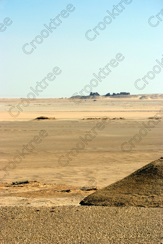 Soknopaiou Nesos fm Desert 6535EG07JHP 
 Soknopaiou Nesos Ruins Desert Dimyah al-Siba Ptolemaic Egyptian horizon distant town outline dating through to Roman times built by the shores of Lake Qarun or Moeris, with a substantial mudbrick enclosure wall partially buried surrounding the remains of a temple dedicated to Soknopaios, a form of the crocodile God Sobek. It is located in the western desert south of Cairo and is accessed by 4x4 from Faiyum and is often part of a desert trip including Qasr al-Saghah Temple here viewed on approach over the desert track from the Lake. 
 Keywords: Egypt, Egyptian, Egyptology, el-Fayoum, Fayyum, Fayum, Lake Qarun, Moeris, Soknopaiou Nesos, island, Dimyah al-Siba, desert, view, approach, archaeology, ancient, history, upright, digital, Ptolemaic, Ptolemy 11 Philadelphus, Septimius Severus, temple, Suchos, Soknopaios, Sobek, processional, way, mudbrick, enclosure, walls, layering, pan, bedding, hot, sand, blistering, heat, sun, blue, sky, angle, eroded, stones