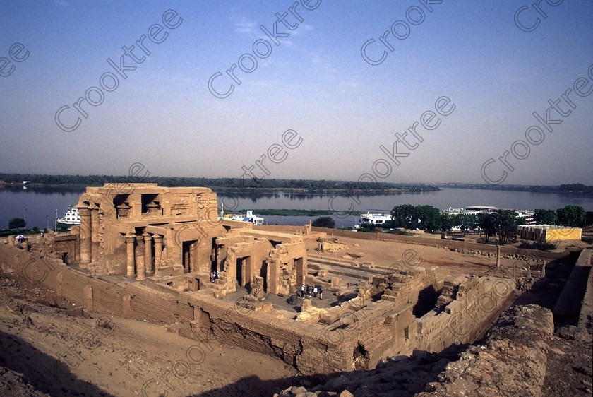 Kom Ombo EG20433jhp 
 Kom Ombo Temple Nile Egyptian rare high view downstream overview of this beautiful ruined temple just north of Aswan and a regular visit on all Nile Cruises, was principally built by Ptolemy V of Silsilah sandstone. Dedicated to two Gods  Sobek, the crocodile and Horus, the falcon and although it has been damaged over the years, mainly through slipping into the River Nile and some structural damage owing to earthquakes, there are still some wonderful colourful reliefs of the most detailed and delicate style. This trip was special for me in that I got special permission to climb up the back of the temple on the hill behind and match a view I had on a Victorian albumen print; the local Police Chief had to be involved and thanks to a good Kuoni Guide he agreed for me to be accompanied by a policemen as security was still a big thing after the 1997 attacks at Luxor. Unfortunately in the excitement I had forgot to adjust my ASA rating for Velvia and took the photos based on 400ASA-the film maws later pushed to 200asa so there is some increase in grain structure, not a feature of Velvia generally. On this visit some cleaning and restoration was being done to the many painted bas reliefs on the columns-hence the scaffolding and the sun umbrella but the bonus was the reliefs looked particularly vibrant. The time of day also meant some of the museum blocks with deep cut carvings were ideal to photograph as the shadows gave greater emphasis to the excellent cut marks of some iconic hieroglyphic symbols. 
 Keywords: Egypt, East Bank, River Nile, Kom Ombo, Temple, summer, morning, hypostyle hall, pylon, columns, bas, reliefs, restoration, cleaning, conservation, coloured, colored, colours, colors, Silsilah, sandstone, landscape, history, archaeology, ancient, Egyptian, Egyptology, crocodiles, Ptolemaic, Ptolemy, Horus, Haroeris, Harwer, Sobek, Hathor, carvings, detailed, delicate, beautiful, fine, Velvia, slide, film, scans, scan, scanned, 35mm, Nikon, FM, manual, July, 2000