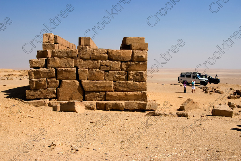 Qasr al-Saghah Temple 6588EG07JHP 
 Qasr al-Saghah Temple Visitors 4x4 Desert Vehicle Police Escort Tour Sand at a small late 12th century Egyptian worker's temple, unfinished and uninscribed near the Gebel el-Qatrani worker’s town servicing the basalt mines to the west of Lake Qarun and accessible only by 4x4 on specialist tours of Egypt. It is constructed of dark brown calciferous sandstone with seven cult shrines facing a common offering table room with the probable front of the temple never finished. 
 Keywords: Egypt, Egyptian, Egyptology, al-Siba, Qasr el-Sagha, al-Saghah, Es-Saghah, Temple, seven, cult, shrines, crypt, offering, table, room, Sobek, archaeology, ancient, history, landscape, 4x4, desert, safari, calciferous, sandstone, sand, blistering, heat, sun, blue, sky, eroded, stones, foreground, hills, stratified, erosion