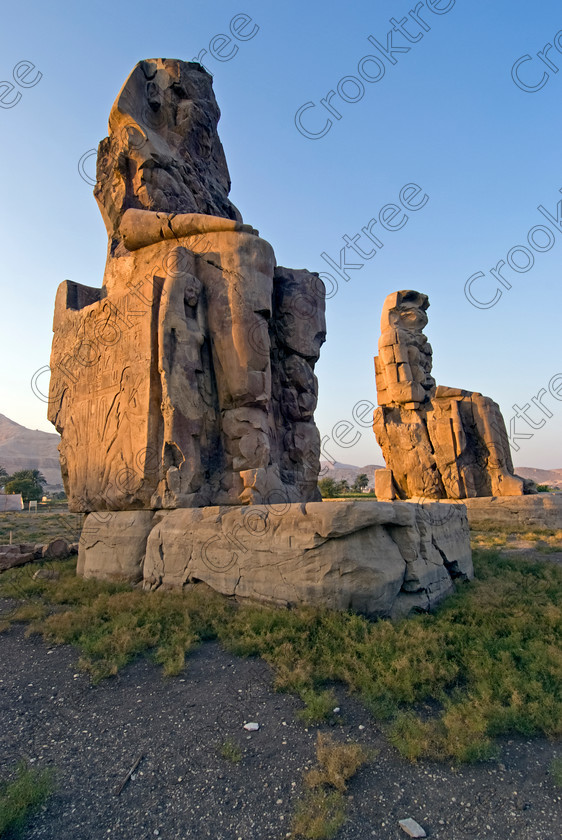 Colossi Memnon Luxor EG075305jhp 
 Colossi Memnon statues seated sunset Egyptian evening Luxor Amenophis mortuary temple that are the most famous remains of his mortuary temple on the northern side of the approach road for the Valley of the Kings, Queens and all the other main West Bank sites. It is the visitors first site of major impact, not far from the main ticket office but is usually visited as a photo opportunity on leaving - recent excavations of the site are finding many hidden buildings and artefacts as well as defining the whole of the remains of the temple complex. 
 Keywords: Egypt, Egyptian, Luxor, West, Bank, Thebes, Theban, hills, fields, River, Nile, upright, history, archaeology, ancient, Egyptology, Amenhotep, Amenophis, Pharaoh, Tiye, Queen, Mother, mortuary, temple, Colossi, Memnon, seated, statues, side, panels, Union, Upper, Lower, earthquake, damaged, repairs, Severus, sunset, glow, roadside, coachstop, excavations