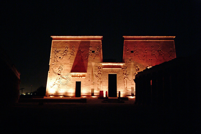 Aswan Philae Light Show EG02933jhp 
 Philae Light Show Aswan Egyptian red orange colours Pylon courtyard in which, during the first section, spectators walk through the temple with areas highlighted at each stop but the time to take photographs is limited. The second part of the evening is seated and photography is very easy, a tripod is permitted and necessary for time exposures to be made as flash on cameras is almost pointless and more of a nuisance for other viewers. This Sound & Light Show is perhaps the most spiritual of those shown at other centres especially with the trip at night by boat to the island and the peacefulness that naturally surrounds this location. 
 Keywords: Egypt, Aswan, River, Nile, Nubia, Agilkia, Philae, Temple, landscape, first, pylon, pylons, Trajan, Kiosk, stele, Ptolemaic, Island, Sound, Light, Son, Lumiere, surreal, experience, spectacular, fantasy, dramatic, colours, colors, red, orange, yellow, colourful, colorful, history, antiquity, ancient, Egyptian, walk, through, sitting, dark, night, stars, holiday, travel, tourists, tourism, boat, water, Egyptology, entrance, courtyard, colonnades, 2002, Fuji, S2, DSLR
