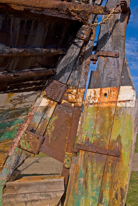 Burghead Old Trawler UP290393JHP 
 Scottish Old Trawler Rusty Rudder Flaking Paint Beached Exhibit Rust Wood possibly for repair, but showing the signs of a hard life at sea with rust and corrosion but a photographer’s dream with all the colours, patterns and textures of weathered paint and the shape of the ship form so accessible. Burghead is a fishing port on the Morayshire coast near Elgin and with a historical importance as a former Pictish stronghold, one of largest forts in Scotland. 
 Keywords: Scotland, Scottish, Moray Firth, Morayshire, upright, heritage, trail, Burghead, harbour, coast, trawler, old, fishing, boat, beached, repairs, rudder, rust, corrosion, wooden, patterns, shapes, texture, colours, colors, weathered, curling
