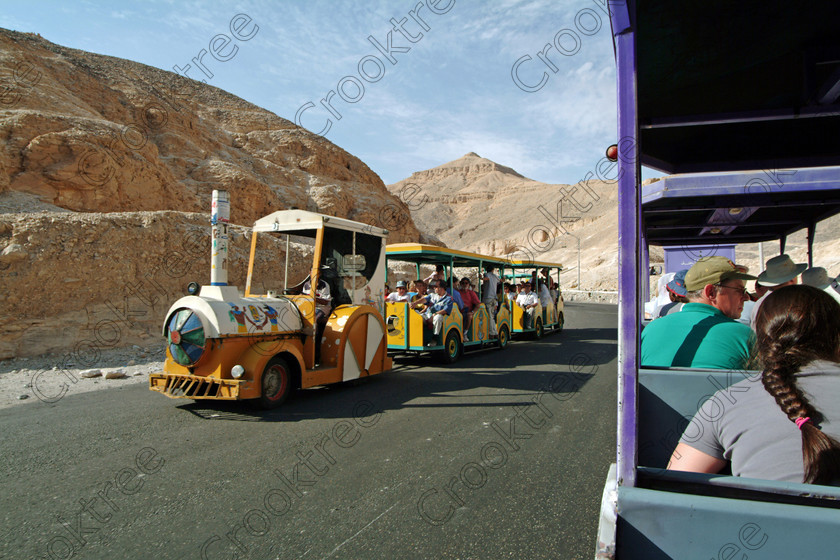 Valley Kings Train EG02038jhp 
 Egypt Luxor Valley Kings Tombs coachpark transport trains visitors tourists considered a more environmentally acceptable way of transporting tourists from the coaches into one of the most visited places in the world probably and certainly in Egypt is this desolate desert valley beneath the Theban mountain on the West Bank of the River Nile at Luxor famous for some of the most important Royal burials of this ancient civilisation. It is possible to climb over the hills above the Valley, pass above the huge amphitheatre of Deir el-Bahri above Hatshepsuts spectacular Mortuary Temple and come down into Deir el-Medina, the workers village using the same paths as they must have done over 3000 years ago. 
 Keywords: Egypt, Egyptian, Luxor, West, Bank, Thebes, Theban, hill, mountain, Valley, Kings, pharaoh, tombs, landscape, ancient, Egyptian, archaeology, Egyptology, shelters, transport, trains, entrances, desert, rocky, sand, heat, exposed, isolated, desolate, crowds, visitors, tourists, busy, colourful