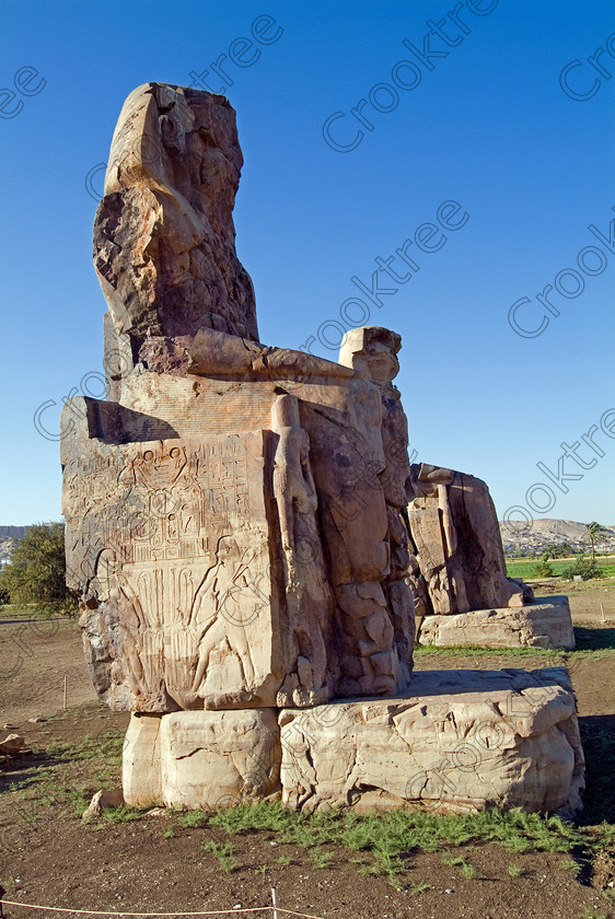 Colossi of Memnon EG051934JHP 
 Colossi Memnon closeup photo upright seated statues West Bank Nile Luxor are of Amenhotep 111 that are the most famous remains of his mortuary temple on the northern side of the approach road for the Valley of the Kings, Queens and all the other main West Bank sites. It is the visitors’ first site of major impact, not far from the main ticket office but is usually visited as a photo opportunity on leaving - recent excavations of the site are finding many hidden buildings and artefacts. 
 Keywords: Egypt, Egyptian, Luxor, West Bank, Thebes, Theban, hills, River Nile, Colossi of Memnon, seated, statues, Amenhotep, Pharaoh, side, relief, union, upper, lower, Hapi, tying, lotus, papyrus, upright, history, archaeology, ancient, Egyptology, temple, roadside, coachstop, excavations, farmland