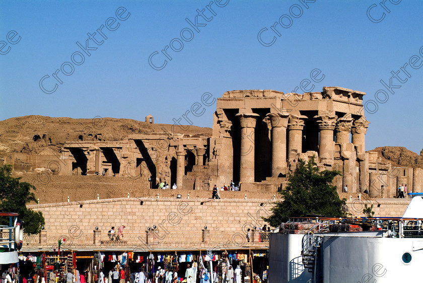 Kom Ombo Temple EG052450JHP 
 Kom Ombo Ptolemaic Full Side Temple Mudbrick Enclosure Wall Berth View viewed from the cruiseboat on the River Nile just north of Aswan and a regular visit on all Nile Cruises, was principally built by Ptolemy V of Silsilah sandstone. Dedicated to two Gods – Sobek, the crocodile and Horus, the falcon and although it has been damaged over the years, mainly through slipping into the River Nile and some structural damage owing to earthquakes, there are still some wonderful colourful reliefs of the most detailed and delicate style. 
 Keywords: Egypt, East Bank, River Nile, Kom Ombo, Temple, hypostyle hall, columns, floral, capitals, mudbrick, enclosure, traders, bas reliefs, coloured, colored, colours, colors, Silsilah, sandstone, landscape, history, archaeology, ancient, Egyptian, Egyptology, crocodiles, Ptolemaic, carvings, detailed, delicate, beautiful, fine