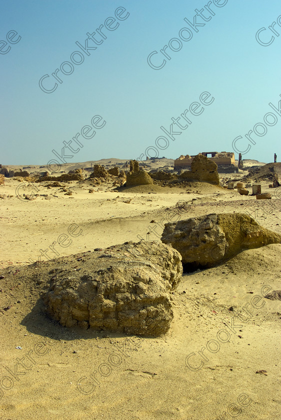 Karanis nr Southern Temple 6438EG07JHP 
 Karanis Kom Aushim City Fayoum Egypt Ptolemaic Roman Mudbrick Erosion in the north eastern edge of the oasis area known as Fayoum and dates from Ptolemaic times through to 500AD. Two Roman dated temples survive in reasonable state and the southern one is dedicated to the crocodile Gods of Pnepheros and Petesuchos. Many finds have been made especially of life in a residential area with houses scattered throughout the site and there is also a fine Roman bathhouse. A small museum now closed has been replaced with an open air area with a selection of artefacts adjacent to the main walk to the temples as this photos shows as we approach the Southern Temple to the right 
 Keywords: Egypt, Egyptian, Egyptology, upright, Karanis, Kom Aushim, el-Fayoum, Faiyum, Fayyum, Nero, Claudius, Vespasiun, Roman Emperors, walk, approach, mudbrick, wall, South temple, outer, construction, foundations, gods, crocodile, dedicated, local, Pnepheros, Petesouchus, desert, sand