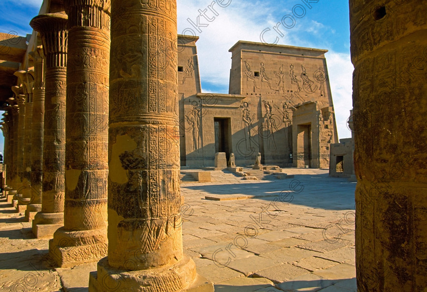 Philae Temple of Isis EG02233JHP 
 Egyptian Philae Temple West Colonnade Framing Coutyard Pyon Entrance home of the Goddess Isis was established late in the history of Egypt being mainly Ptolemaic, eventually closing as a religious site around 550AD and being located on an island had remained remarkably untouched. Being relocated onto the Island of Agilkia on the River Nile near Aswan, to save it being flooded after the completion of the High Dam, it is perhaps one of the loveliest and most complete classic Egyptian temples to visit with a peaceful spirituality lacking in many of the land based sites. 
 Keywords: Egypt, Aswan, River Nile, Nubia, Philae Temple, island, pylon, first, entrance, court, early, morning, shadows, colonnade, western, landscape, upright, history, ancient, Egyptian, antiquity, archaeology, Egyptology, Agilkia Island, slide, scanned