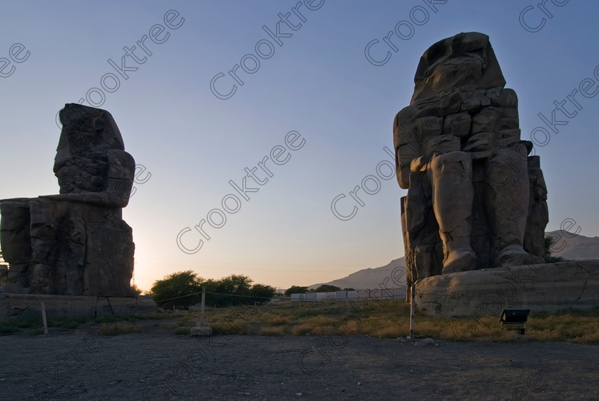Colossi Memnon Luxor EG075303jhp 
 Colossi Memnon statues seated sunset silhouettes Amenhotep Egyptian Luxor mortuary temple that are the most famous remains of his mortuary temple on the northern side of the approach road for the Valley of the Kings, Queens and all the other main West Bank sites. It is the visitors first site of major impact, not far from the main ticket office but is usually visited as a photo opportunity on leaving - recent excavations of the site are finding many hidden buildings and artefacts as well as defining the whole of the remains of the temple complex. 
 Keywords: Egypt, Egyptian, Luxor, West, Bank, Thebes, Theban, hills, fields, River, Nile, landscape, history, archaeology, ancient, Egyptology, Amenhotep, Amenophis, Pharaoh, Tiye, Queen, Mother, mortuary, temple, Colossi, Memnon, seated, statues, side, panels, Union, Upper, Lower, earthquake, damaged, repairs, Severus, sunset, glow, roadside, coachstop, excavations