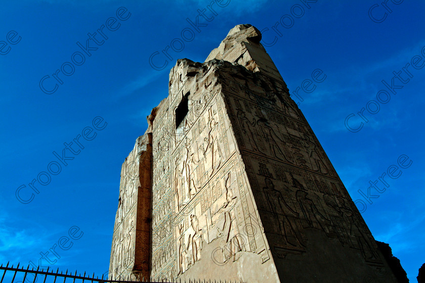 Kom Ombo Pylon EG02456JHP 
 Kom Ombo Ancient Egypt Temple Pylon Carved Blue Sky Perspective Upwards on the River Nile just north of Aswan and a regular visit on all Nile Cruises, was principally built by Ptolemy V of Silsilah sandstone. Dedicated to two Gods – Sobek, the crocodile and Horus, the falcon and although it has been damaged over the years, mainly through slipping into the River Nile and some structural damage owing to earthquakes, there are still some wonderful colourful reliefs of the most detailed and delicate style. 
 Keywords: Egypt, East Bank, River Nile, Kom Ombo, Temple, hypostyle hall, pylon, columns, bas reliefs, coloured, colored, colours, colors, Silsilah, sandstone, landscape, damaged, history, archaeology, ancient, Egyptian, Egyptology, Ptolemaic, Ptolemy, Horus, Haroeris, Harwer, Sobek, Hathor, carvings, detailed, delicate, beautiful, fine