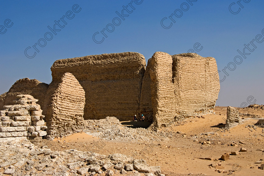 Soknopaiou Nesos Enclosure Wall 6555EG07JHP 
 Soknopaiou Nesos Ruins Dimyah al-Siba Walls Mudbrick Panning Pan Layering at this Ptolemaic town dating through to Roman times built by the shores of Lake Qarun or Moeris, with a substantial mudbrick enclosure wall partially buried as seen in this photo, surrounding the remains of a temple dedicated to Soknopaios, a form of the crocodile God Sobek. It is located in the western desert south of Cairo and is accessed by 4x4 from Faiyum and is often part of a desert trip including Qasr al-Saghah Temple. 
 Keywords: Egypt, Egyptian, Egyptology, el-Fayoum, Fayyum, Fayum, Lake Qarun, Moeris, Soknopaiou Nesos, island, Dimyah al-Siba, archaeology, ancient, history, landscape, digital, camera, desert, Ptolemaic, Ptolemy 11 Philadelphus, Septimius Severus, temple, Suchos, Soknopaios, Sobek, processional, way, mudbrick, enclosure, walls, layering, pan, bedding, hot, sand, blistering, heat, sun, blue, sky, angle, eroded, stones