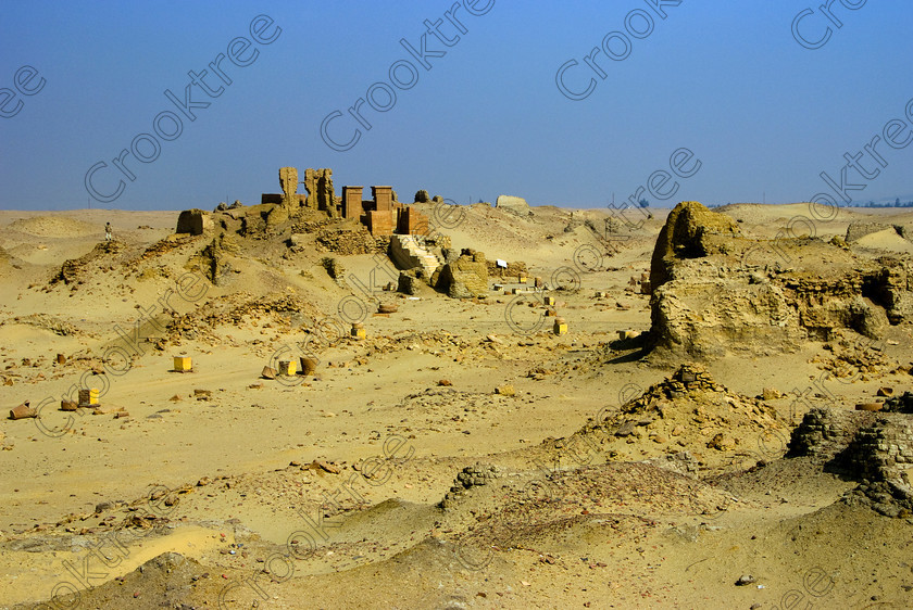 Karanis North Temple 6449EG07JHP 
 Karanis Kom Aushim Egypt North Temple Vista Desert Ruins Mudbrick was a city on the north eastern edge of the area known as Fayoum and dates from Ptolemaic times through to 500AD. Two Roman dated temples survive in reasonable state with this photo showing the north temple viewed from the southern one which was dedicated to the crocodile Gods of Pnepheros and Petesuchos. Many finds have been made especially of life in a residential area with houses scattered throughout the site and there is also a fine Roman bathhouse. A small museum now closed has ben replaced with an open air area with a selection of artefacts adjacent to the main walk to the temples. 
 Keywords: Egypt, Egyptian, Egyptology, landscape, Karanis, Kom Aushim, el-Fayoum, Faiyum, Fayyum, Nero, Claudius, Vespasiun, Roman Emperors, North temple, ruin, gleaming, shining, surreal, desert, sand