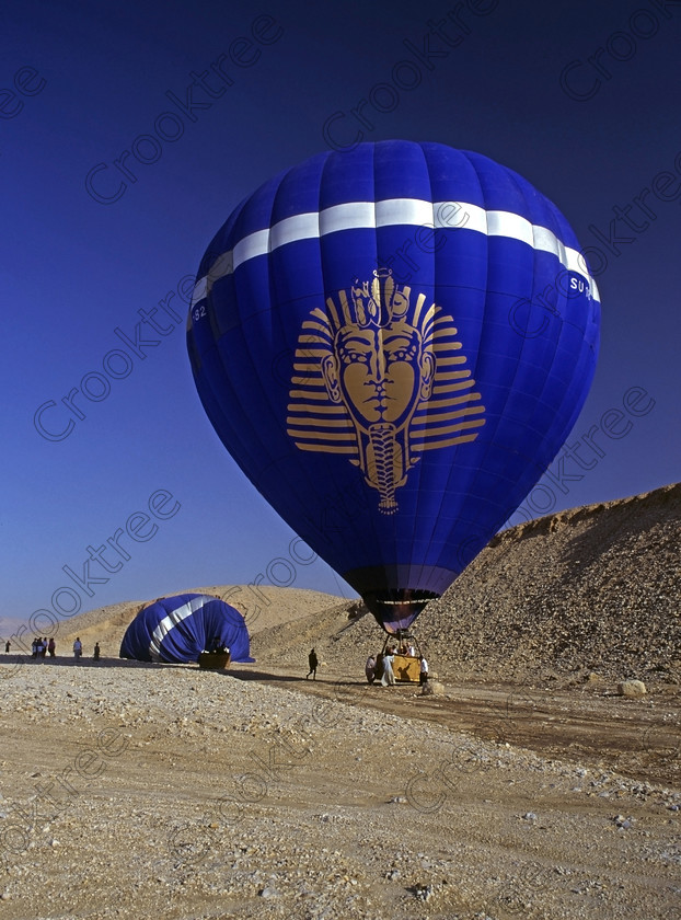 Luxor Balloon EG922411jhp 
 Balloons flight excursion landed desert sand tourists hills Egypt western Luxor pick up. The balloon flight illustrated here was in 1994 and there were only two although in later years these increased greatly in numbers. This trip took off from the front of Hatshepsut just after dawn, a cold and interesting crossing of the Nile in the dark and long before the modern road bridge and eventually landed in the desert where the Hilton Hotel put on a beautiful breakfast buffet. 
 Keywords: Egypt, Egyptian, Luxor, Ramasseum, Temple, West, Bank, River Nile, Thebes, Qurnat, Murai, Shaykh 'Abd al-Qurnah, landscape, upright, Western, desert, sand, stones, sunlight, dawn, agriculture, farming, houses, tombs, Nobles, high, panorama, balloon, balloons, landed, tourists, collected, basket, motif, face, blue, silver, 1994, slide, film, 645, medium, format, transparency, scanned, scan, Bronica, ETRSi