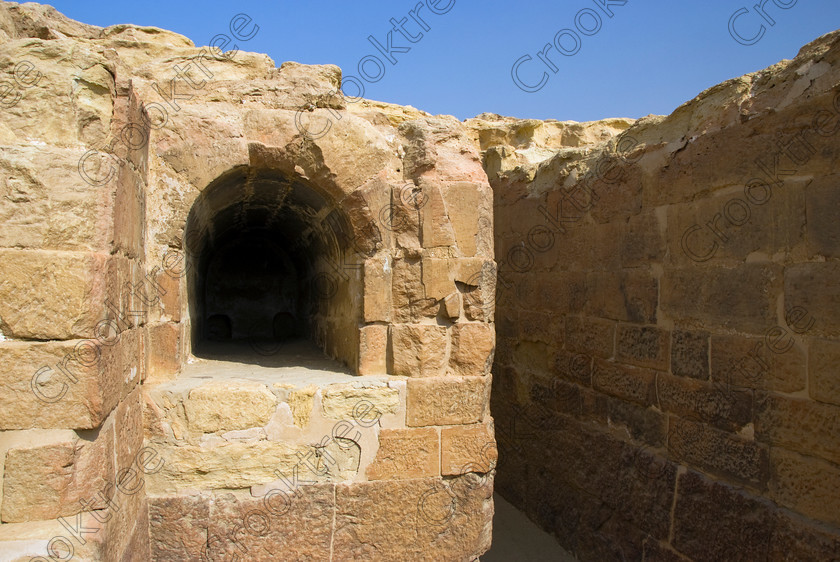 Karanis Temple Burial 6448EG07JHP 
 Karanis Kom Aushim Southern Egyptian Temple Coffin Crypt Interior Photo was a city on the north eastern edge of the area known as Fayoum and dates from Ptolemaic times through to 500AD. Two Roman dated temples survive in reasonable state and the southern one in which this photo shows a crypt in which to hold a coffin is dedicated to the crocodile Gods of Pnepheros and Petesuchos. Many finds have been made especially of life in a residential area with houses scattered throughout the site and there is also a fine Roman bathhouse. A small museum now closed has ben replaced with an open air area with a selection of artefacts adjacent to the main walk to the temples. 
 Keywords: Egypt, Egyptian, Egyptology, landscape, Karanis, Kom Aushim, el-Fayoum, Faiyum, Fayyum, Nero, Claudius, Vespasiun, Roman Emperors, South temple, burial, coffin, crypt, outer, wall, construction, foundations, gods, crocodile, dedicated, local, Pnepheros, Petesouchus, desert, sand