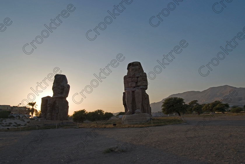 Colossi of Memnon Sunset 5301EG07JHP 
 Colossi Memnon silhouette sunset photograph Egyptian West Bank Nile Luxor are two ruined seated statues of Amenhotep 111 that are the most famous remains of his mortuary temple on the northern side of the approach road for the Valley of the Kings, Queens and all the other main West Bank sites. It is the visitors first site of major impact, not far from the main ticket office but is usually visited as a photo opportunity on leaving - recent excavations of the site are finding many hidden buildings and artefacts. 
 Keywords: Egypt, Egyptian, Luxor, West, Bank, Thebes, Theban, River Nile, landscape, history, archaeology, ancient, Egyptology, temples, Colossi, Memnon, sunset, silhouette, roadside, coachstop, excavations, palm, tree