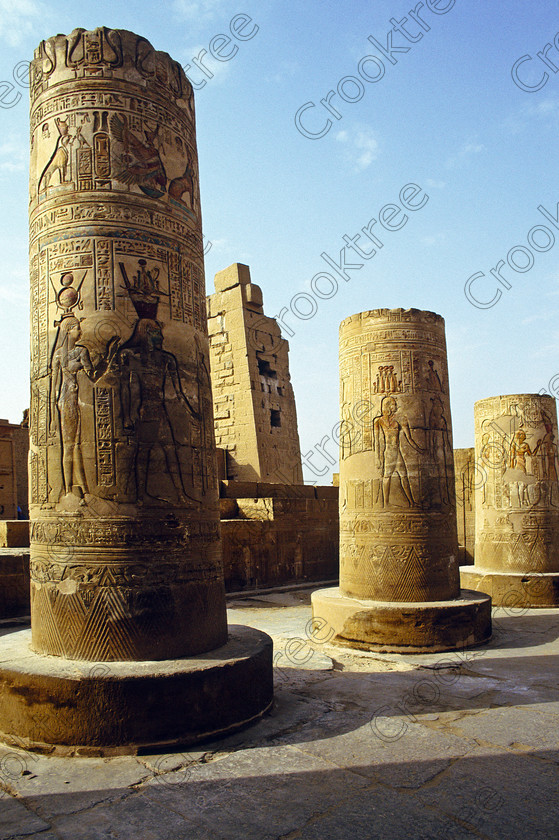 Kom Ombo EG204315jhp 
 Kom Ombo Temple Nile Egypt columns broken colours painted carvings pylon of this beautiful ruined temple just north of Aswan and a regular visit on all Nile Cruises, was principally built by Ptolemy V of Silsilah sandstone. Dedicated to two Gods  Sobek, the crocodile and Horus, the falcon and although it has been damaged over the years, mainly through slipping into the River Nile and some structural damage owing to earthquakes, there are still some wonderful colourful reliefs of the most detailed and delicate style. This trip was special for me in that I got special permission to climb up the back of the temple on the hill behind and match a view I had on a Victorian albumen print; the local Police Chief had to be involved and thanks to a good Kuoni Guide he agreed for me to be accompanied by a policemen as security was still a big thing after the 1997 attacks at Luxor. Unfortunately in the excitement I had forgot to adjust my ASA rating for Velvia and took the photos based on 400ASA-the film maws later pushed to 200asa so there is some increase in grain structure, not a feature of Velvia generally. On this visit some cleaning and restoration was being done to the many painted bas reliefs on the columns-hence the scaffolding and the sun umbrella but the bonus was the reliefs looked particularly vibrant. The time of day also meant some of the museum blocks with deep cut carvings were ideal to photograph as the shadows gave greater emphasis to the excellent cut marks of some iconic hieroglyphic symbols. 
 Keywords: Egypt, East Bank, River Nile, Kom Ombo, Temple, summer, morning, hypostyle hall, pylon, columns, bas, reliefs, restoration, cleaning, conservation, coloured, colored, colours, colors, Silsilah, sandstone, landscape, upright, history, archaeology, ancient, Egyptian, Egyptology, crocodiles, Ptolemaic, Ptolemy, Horus, Haroeris, Harwer, Sobek, Hathor, carvings, detailed, delicate, beautiful, fine, Velvia, slide, film, scans, scan, scanned, 35mm, Nikon, FM, manual, July, 2000