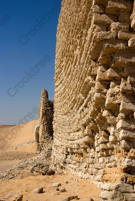 Soknopaiou Nesos Pan Bedding 6563EG07JHP 
 Soknopaiou Nesos Ruins Egyptian Mudbrick Walls Pan Layering Ptolemaic town dating through to Roman times built by the shores of Lake Qarun or Moeris, with a substantial mudbrick enclosure wall partially buried surrounding the remains of a temple dedicated to Soknopaios, a form of the crocodile God Sobek. It is located in the western desert south of Cairo and is accessed by 4x4 from Faiyum and is often part of a desert trip including Qasr al-Saghah Temple. This photo illustrates pan bedding where a mudbrick wall fallows the contours of the ground on which it is built. 
 Keywords: Egypt, Egyptian, Egyptology, el-Fayoum, Fayyum, Fayum, Lake Qarun, Moeris, Soknopaiou Nesos, island, Dimyah al-Siba, archaeology, ancient, history, upright, digital, camera, desert, Ptolemaic, Ptolemy 11 Philadelphus, Septimius Severus, temple, Suchos, Soknopaios, Sobek, processional, way, mudbrick, enclosure, walls, layering, pan, bedding, hot, sand, blistering, heat, sun, blue, sky, angle, eroded, stones