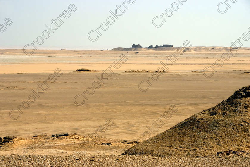 Soknopaiou Nesos fm Desert 6534EG07JHP 
 Soknopaiou Nesos Ruins Dimyah al-Siba Ptolemaic town Egyptian Desert Photograph dating through to Roman times built by the shores of Lake Qarun or Moeris, with a substantial mudbrick enclosure wall partially buried surrounding the remains of a temple dedicated to Soknopaios, a form of the crocodile God Sobek. It is located in the western desert south of Cairo and is accessed by 4x4 from Faiyum and is often part of a desert trip including Qasr al-Saghah Temple here viewed on approach over the desert track from the Lake. 
 Keywords: Egypt, Egyptian, Egyptology, el-Fayoum, Fayyum, Fayum, Lake Qarun, Moeris, Soknopaiou Nesos, island, Dimyah al-Siba, archaeology, ancient, history, landscape, digital, camera, desert, Ptolemaic, Ptolemy 11 Philadelphus, Septimius Severus, temple, Suchos, Soknopaios, Sobek, processional, way, mudbrick, enclosure, walls, layering, pan, bedding, hot, sand, blistering, heat, sun, blue, sky, angle, eroded, stones