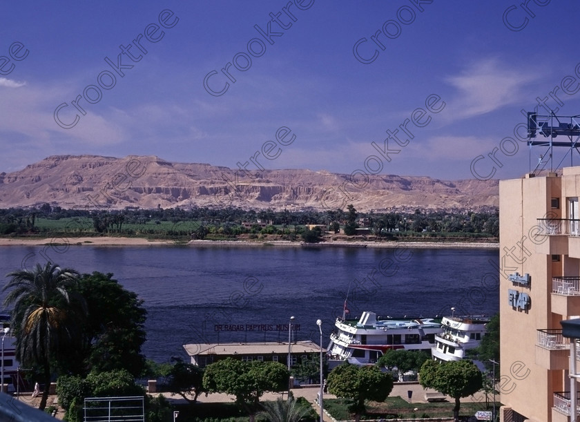 Luxor View EG945113jhp 
 Egypt Luxor Mercure Etap Hotel River Nile View West Bank Hatshepsut looking over the shimmering River Nile on a sunny September afternoon from one of the riverside balconies of this long standing central Luxor Hotel on the city waterfront. This was my first visit to Luxor and I was lucky to get changed to a room in the north wing which was considerably quieter than one in the centre of the hotel above the swimming pool, various restaurants and a dance floor. It also offered great views to the West Bank. In 1994 the Hotel was the Etap but is now the Mercure and has a great location on the promenade with easy access by foot to the Luxor Museum, to public ferry points for crossing the Nile and to nearby shops or just enjoyed a leisurely walk along the tree lined waterfront by the berthed cruiseboats and feluccas. 
 Keywords: Egypt, Thebes, Luxor, Waset, Ipetisut, East, Bank, River, Nile, Mercure, Etap, Hotel, riverside, riverbank, West, bank, Hatshepsut, temple, balloons, landscape, palm, trees, water, shimmering, September, morning, dawn, sunshine, blue, sky, hazy, Theban, hills, waterfront, promenade, esplanade, modern, architecture, style, stylish, balconies, balcony, tree-lined, papyrus, cruiseboats, berthed, 1994, slide, film, 645, medium, format, transparency, Bronica, ETRSi, scanned, scan