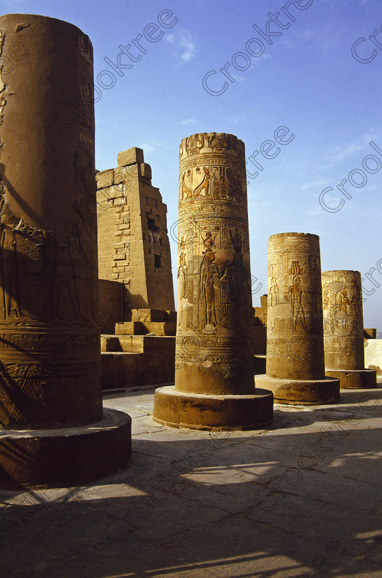 Kom Ombo EG204313jhp 
 Kom Ombo Temple Nile Egyptian columns broken restored painted carvings of this beautiful ruined temple just north of Aswan and a regular visit on all Nile Cruises, was principally built by Ptolemy V of Silsilah sandstone. Dedicated to two Gods  Sobek, the crocodile and Horus, the falcon and although it has been damaged over the years, mainly through slipping into the River Nile and some structural damage owing to earthquakes, there are still some wonderful colourful reliefs of the most detailed and delicate style. This trip was special for me in that I got special permission to climb up the back of the temple on the hill behind and match a view I had on a Victorian albumen print; the local Police Chief had to be involved and thanks to a good Kuoni Guide he agreed for me to be accompanied by a policemen as security was still a big thing after the 1997 attacks at Luxor. Unfortunately in the excitement I had forgot to adjust my ASA rating for Velvia and took the photos based on 400ASA-the film maws later pushed to 200asa so there is some increase in grain structure, not a feature of Velvia generally. On this visit some cleaning and restoration was being done to the many painted bas reliefs on the columns-hence the scaffolding and the sun umbrella but the bonus was the reliefs looked particularly vibrant. The time of day also meant some of the museum blocks with deep cut carvings were ideal to photograph as the shadows gave greater emphasis to the excellent cut marks of some iconic hieroglyphic symbols. 
 Keywords: Egypt, East Bank, River Nile, Kom Ombo, Temple, summer, morning, hypostyle hall, pylon, columns, bas, reliefs, restoration, cleaning, conservation, coloured, colored, colours, colors, Silsilah, sandstone, landscape, upright, history, archaeology, ancient, Egyptian, Egyptology, crocodiles, Ptolemaic, Ptolemy, Horus, Haroeris, Harwer, Sobek, Hathor, carvings, detailed, delicate, beautiful, fine, Velvia, slide, film, scans, scan, scanned, 35mm, Nikon, FM, manual, July, 2000