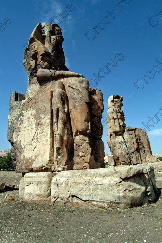 Colossi of Memnon EG020149jhp 
 Colossi Memnon West Bank Luxor two ruined seated statues Amenhotep 111 that are the most famous remains of his mortuary temple on the northern side of the approach road for the Valley of the Kings, Queens and all the other main West Bank sites. It is the visitors first site of major impact, not far from the main ticket office but is usually visited as a photo opportunity on leaving - recent excavations of the site are finding many hidden buildings and artefacts. see Victorian collection for similar viewpoint. 
 Keywords: Egypt, Egyptian, Luxor, West Bank, Thebes, Theban, hills, River Nile, Colossi of Memnon, seated, statues, Amenhotep, Pharaoh, side, relief, union, upper, lower, Hapi, tying, lotus, papyrus, upright, history, archaeology, ancient, then, now, Victorian, Beato, Egyptology, temple, roadside, coachstop, excavations, farmland