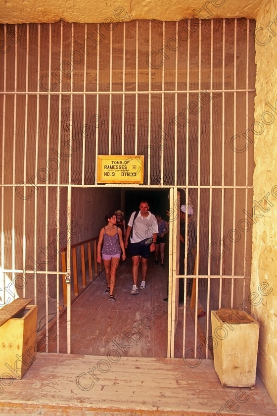 Valley Kings EG006128jhp 
 Egypt Valley Luxor Tomb entrance gate exiting visitors Ramsses V1 after leaving the main collection area resthouses which comes after obtaining tickets at the outer barrier after being transferred by shuttle from the coach park and visitors centre. This is one of the most visited places in the world probably and certainly in Egypt is this desolate desert valley beneath the Theban mountain on the West Bank of the River Nile at Luxor famous for some of the most important Royal burials of this ancient civilisation. It is possible to climb over the hills above the Valley, pass above the huge amphitheatre of Deir el-Bahri above Hatshepsuts spectacular Mortuary Temple and come down into Deir el-Medina, the workers village using the same paths as they must have done over 3000 years ago. 
 Keywords: Egypt, Egyptian, Luxor, West, Bank, Thebes, Theban, hill, mountain, Valley, Kings, pharaoh, tombs, landscape, upright, ancient, Egyptian, archaeology, Egyptology, views, road, shuttle, service, conservation, pollution, prohibition, entrance, tractors, trailers, tracks, shelters, transport, trains, entrances, Tutankhamun, tomb, shelters, rest, house, desert, rocky, sand, heat, exposed, isolated, desolate, crowds, visitors, tourists, busy, 2000, film, slides, Fuji, Velvia, 35mm, scanned, scan, Nikon, FM2, manual