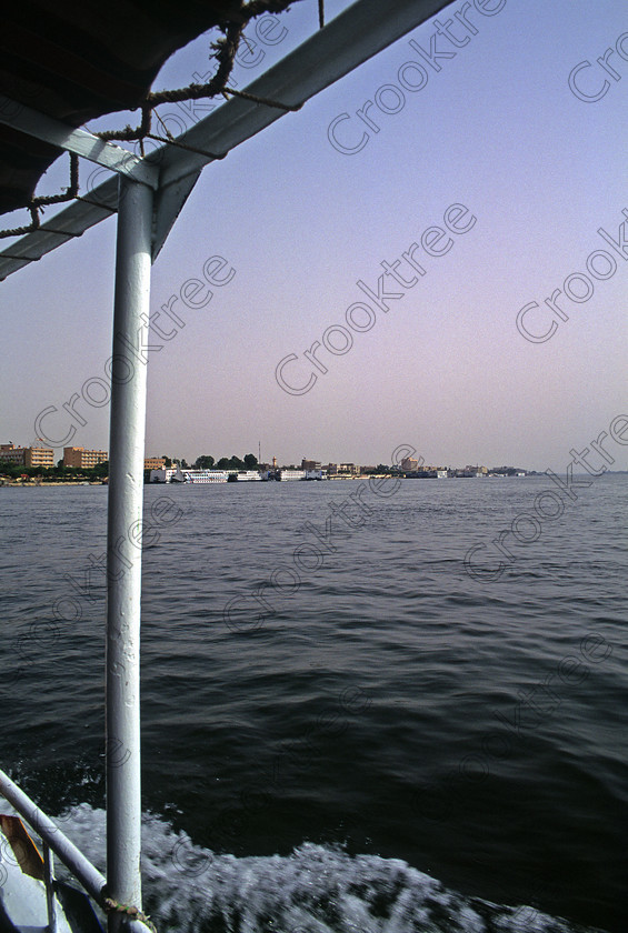 Luxor Nile EG20366jhp 
 Egypt Luxor Hotels River Nile View East Bank ferry crossing downstream and this was the manner of crossing to the West bank from the cruiseboats and hotels in Luxor proper. The road bridge over the Nile slightly to the south of the town was opened in 1998 and then all journeys to the West Bank sites was done by coach and much less romantic than crossing the Nile by ferry boat. It is still possible to use the public ferry and then get a taxi from the ticket office near Qurna al-Gaddah. In 1994 on my first trip I stayed in the Etap Hotel now the Mercure and it was a great location on the promenade, great views over the River with easy access by foot to the Luxor Museum, to public ferry points for crossing the Nile and to nearby shops or just enjoyed a leisurely walk along the tree lined waterfront by the berthed cruiseboats and feluccas. You could see the Temple of Hatshepsut tucked into the Theban hills, watch the balloons starting their early morning flights or see feluccas and cruiseboats sailing along the Nile. In my first few visits to Egypt but especially my first the Nile cruiseboat the RA 11 anchored adjacent to the main promenade and we were collected in the morning by ferryboats and taken over the river to the East Boat and brought back after our visits to the West Bank sites. Coaches were waiting on the West Bank to take us to the sites. 
 Keywords: Egypt, Thebes, Luxor, Waset, Ipetisut, East, Bank, River, Nile, Mercure, Etap, Hotel, hotels, riverside, riverbank, West, bank, ferry, public, crossing, boat, Hatshepsut, temple, balloons, landscape, upright, palm, trees, water, shimmering, morning, sunshine, blue, sky, hazy, Theban, hills, waterfront, promenade, esplanade, modern, architecture, style, stylish, balconies, tree-lined, papyrus, cruiseboats, berthed, 2000, slide, film, 35mm, format, transparency, Fuji, Velvia, Nikon, FM2, scanned, scan